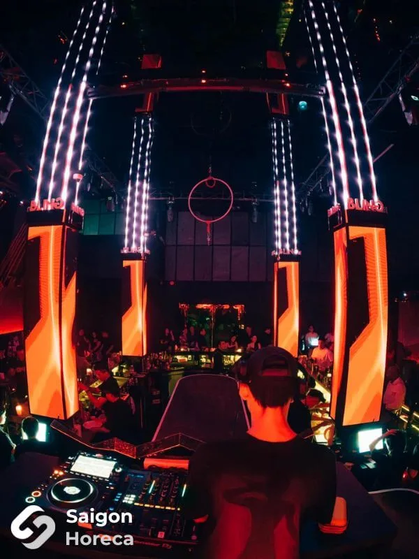 Cabin DJ trình diễn live giữa dàn cột đèn LED cam-đỏ tại Bling Bling Club