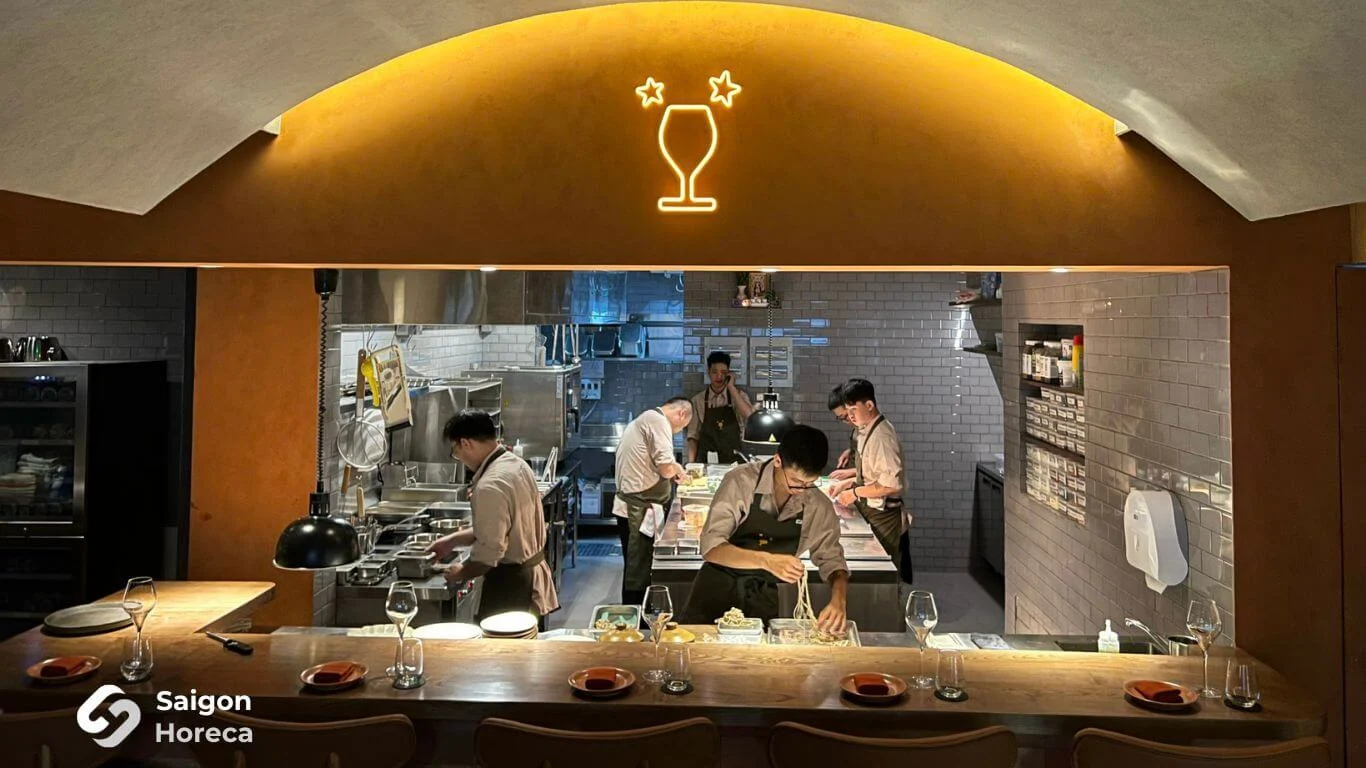 Toàn cảnh ô vòm bếp mở và quầy bar gỗ dài với dàn đầu bếp đang thao tác tại Little Bear Thảo Điền